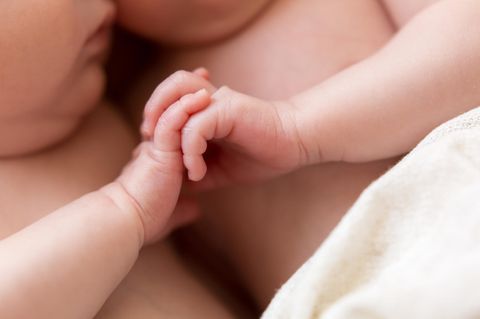 Zwillinge kommen in unterschiedlichen Jahren zur Welt. neugeborene Zwillinge halten Händchen