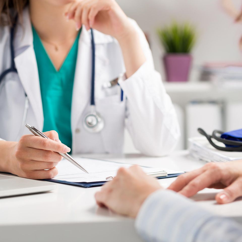 Björn Krause: eine Ärztin sitzt mit einer Patientin an einem Tisch mit einem Stift in der Hand und einem Formular