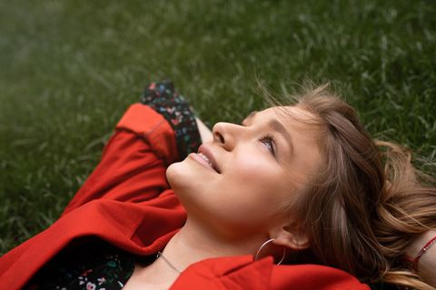 Susanne Kaloff: Eine Frau in roter Jacke liegt mit verschenkten Armen im Gras und schaut in den Himmel