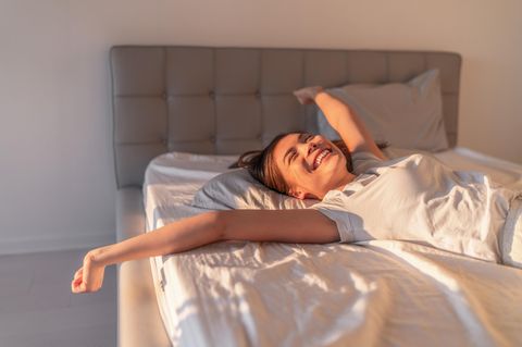 Horoskop: Frau freut sich in ihrem Bett, dass sie ausschlafen konnte