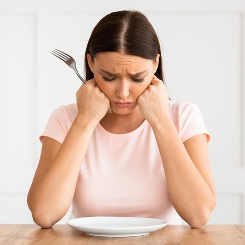 Frau schaut unglücklich auf leeren Teller | Abnehmfallen: Diese 5 Angewohnheiten hemmen deinen Stoffwechsel