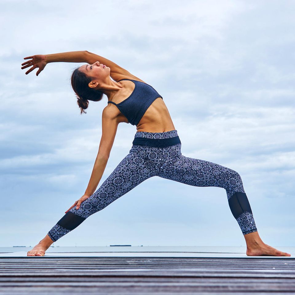 Eine Frau macht auf einem Steg stehend eine Yoga-Übung