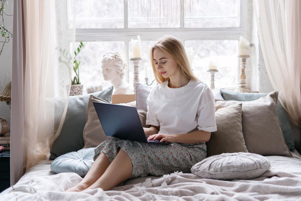 Arbeit aus dem Bett: Eine junge blonde Frau sitzt mit einem Laptop im Bett