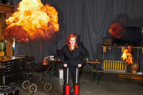 Mebel Hummig: Eine junge Frau mit roten Haaren startet einen Spezialeffekt. Hinter ihr ist eine Feuerwolke
