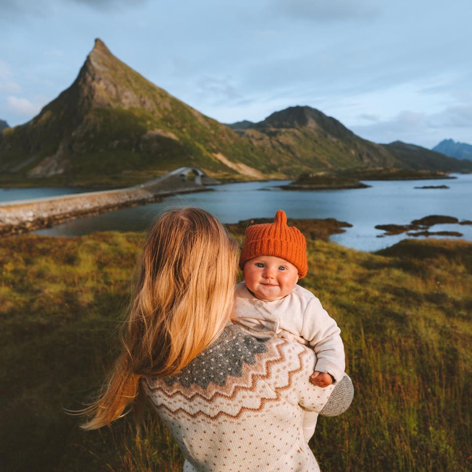 Eine Mutter hält ihr strahlendes Kind in der norwegischen Natur in den Armen.