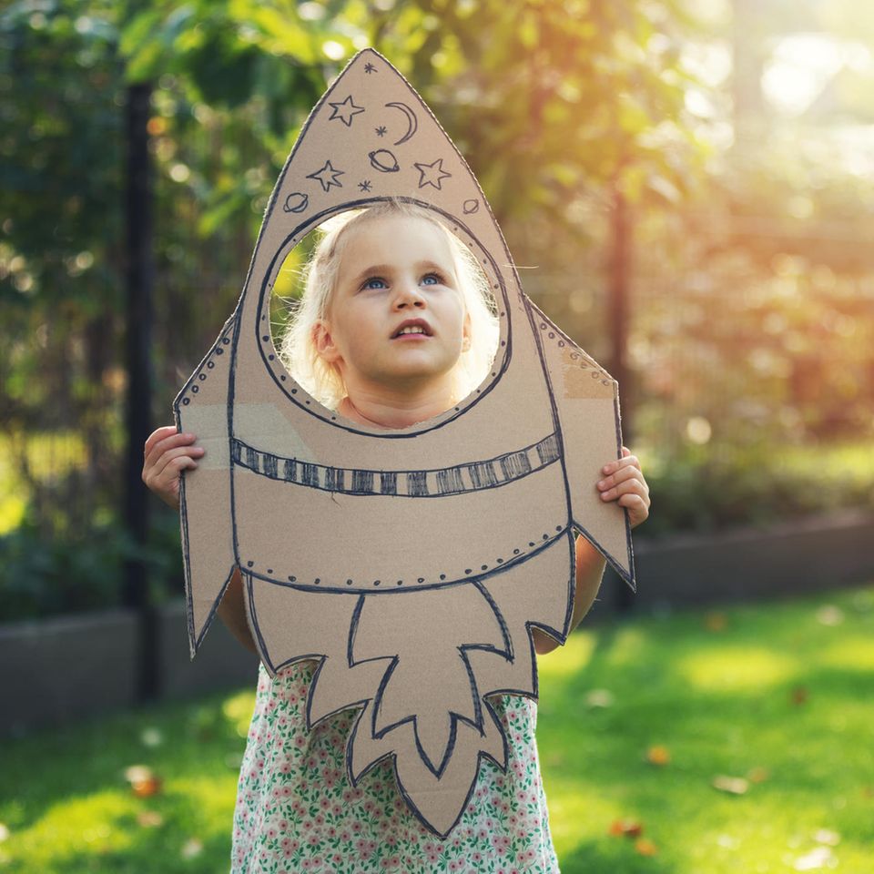 Flug ins All für alle: ein kleines blondes Mädchen hält eine ausgeschnittene Rakete aus Pappe