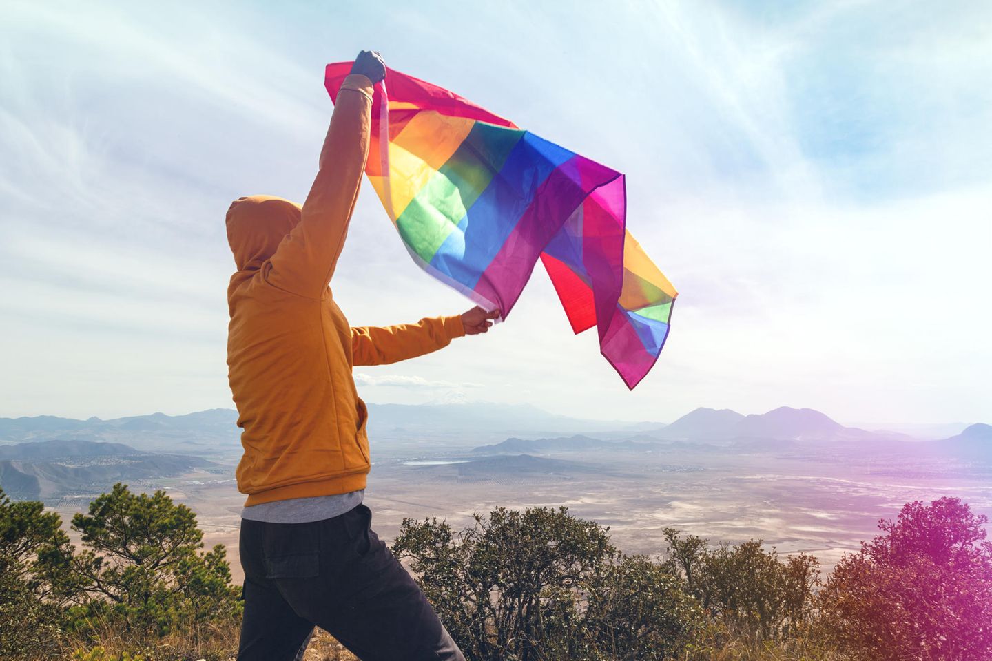 Ein Mann auf einem Hügel schwenkt die LGBTIQ+-Fahne