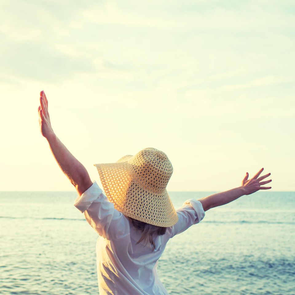 Frau glücklich am Meer | Studie: Brauchen wir doch mehr Geld zum Glücklichsein als gedacht?