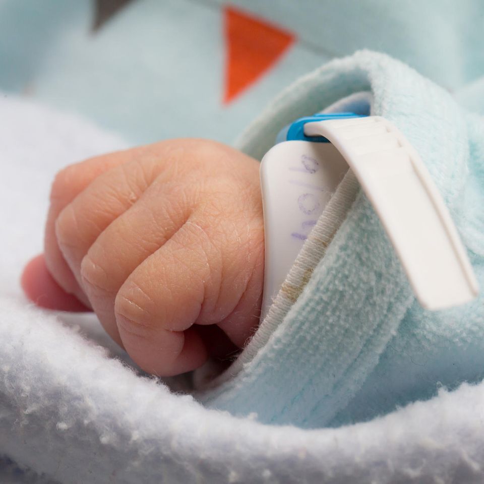 Xyz: die Hand eines neugeborenen Babys. Am Handgelenk ist ein medizinisches Armband sichtbar