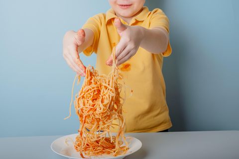 Junge im gelben Shirt spielt mit Spaghetti