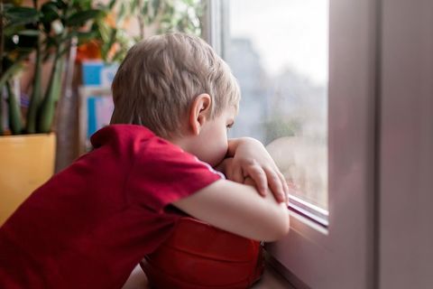 Kind blickt traurig aus dem Fenster
