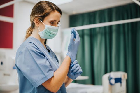Franziska Böhler: eine junge Krankenschwester mit OP Maske zieht sich blaue Handschuhe an