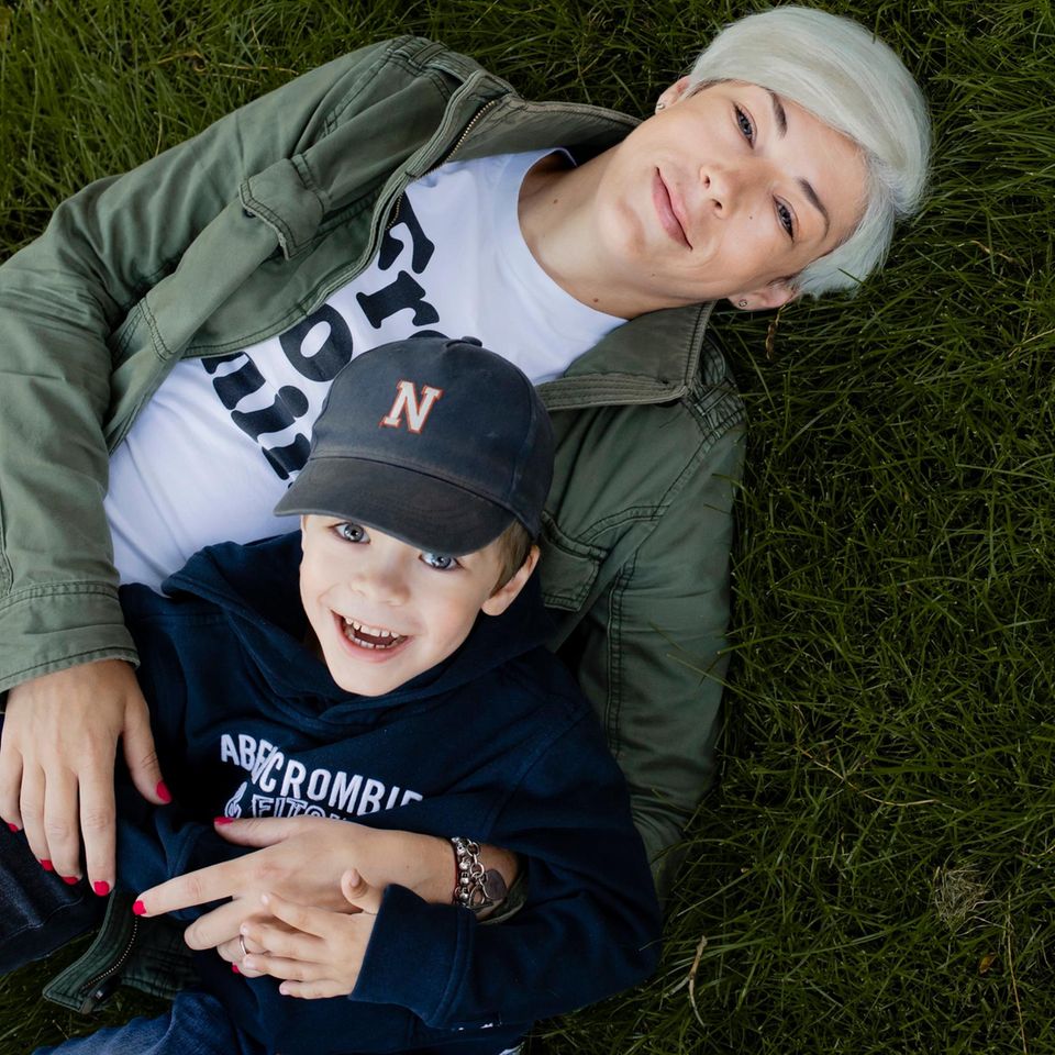 Autistisches Kind: eine junge Mutter mit kurzen platinblonden Haaren liegt mit ihrem jungen Sohn im Gras und gucken hoch