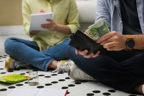 Geld und Liebe: Paar sitzt auf dem Boden und zählt Geld