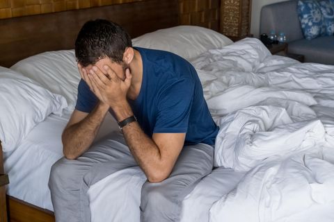 Depression bei Männern: Mann sitzt niedergeschlagen auf Bett