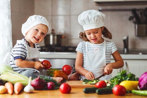 Zwei Kinder kochen mit Gemüse.