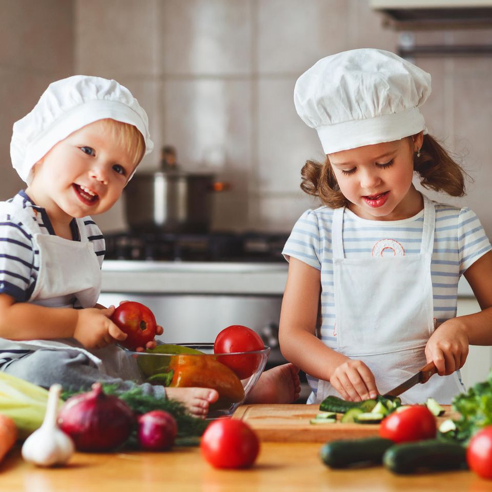 Zwei Kinder kochen mit Gemüse.