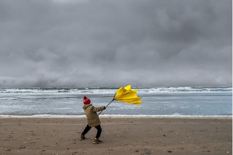 Sturm: Kleiner Junge steht im Sturm am Strand und hält seinen kaputten Regenschirm