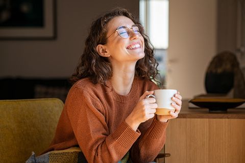 Eine Frau sitzt am Fenster, lacht und hält eine Tasse Tee.