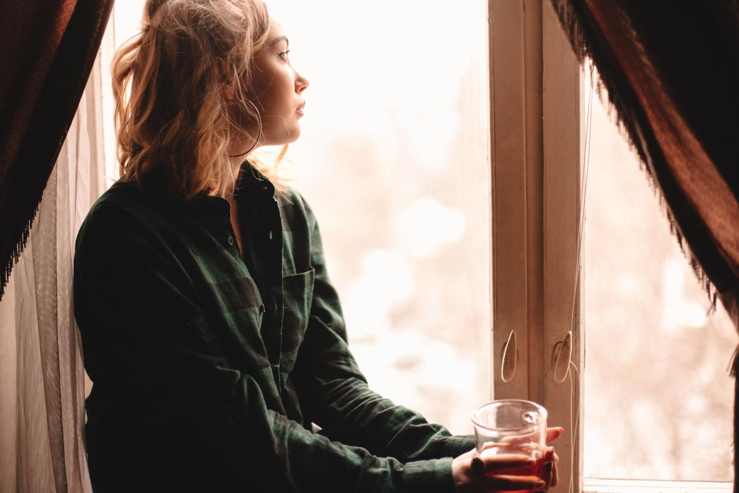Katja Corcoran: eine blonde junge Frau sitzt an einem Fenster und schaut nachdenklich hinaus