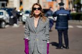 Während das Kostüm von Anna dello Russo einen klassischen Flair versprüht, dürfen ihre Accessoires so richtig knallen. Die roten Lackstiefel in Kombination mit den violetten Handschuhen sorgen dafür, dass der Look der italienischen Modejournalistin definitiv im Gedächtnis bleibt.