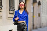 Diese Besucherin der Mailänder Modeschauen behält mit ihrer rosaroten Retro-Sonnenbrille modisch den Durchblick: oben ein azurblauer Cropped-Blazer, unten Lederleggings und Lackstiefel. Das ist edel und rockig zugleich!