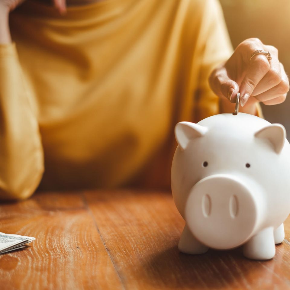 Geldumgang: eine Frau in einem gelben Pullover steckt eine Münze in ein Sparschwein