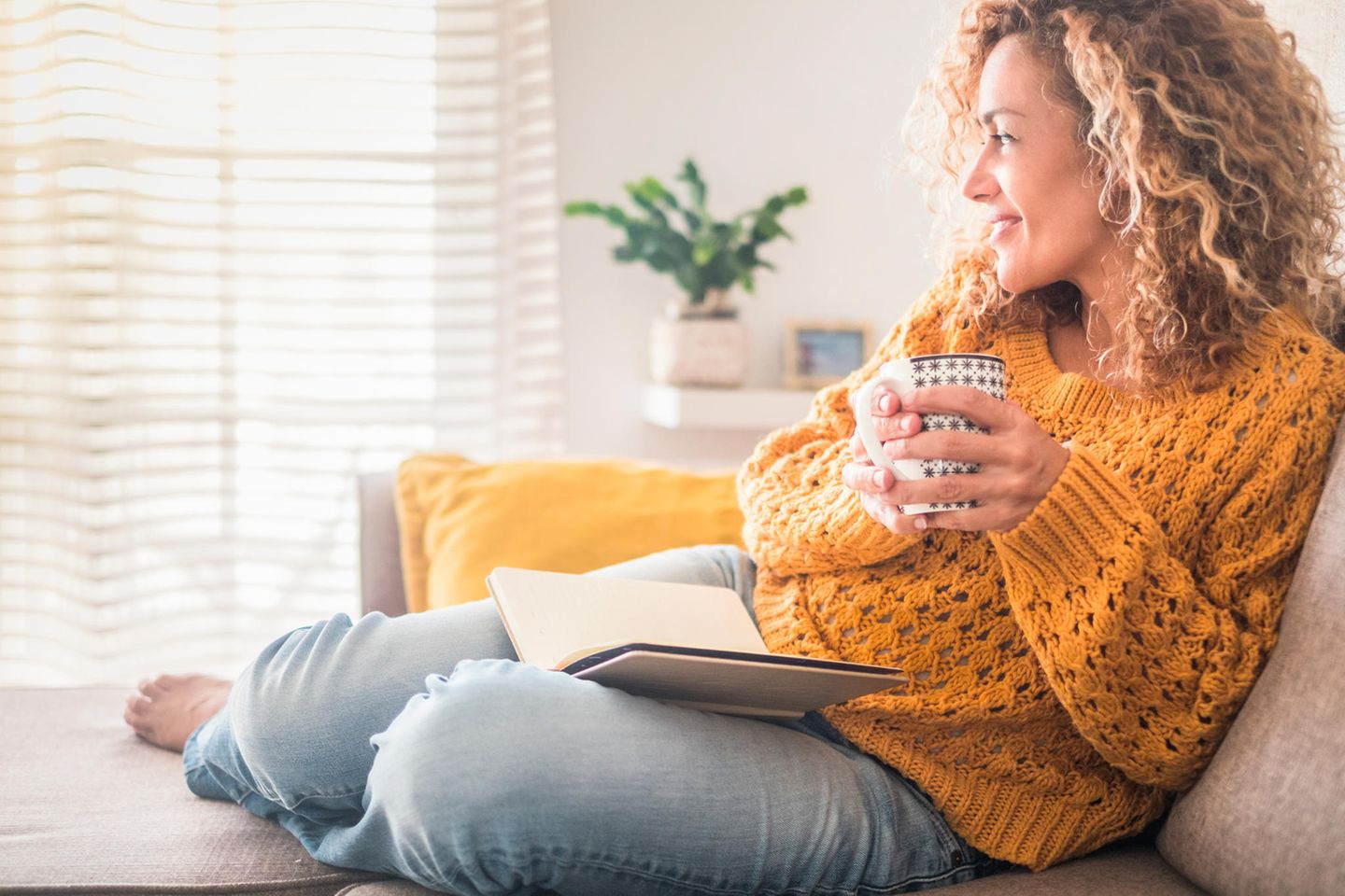 Frau entspannt mit Buch und Tee auf dem Sofa: Die 5 Gehirn-Typen und wie sie dein Glücksempfinden beeinflussen