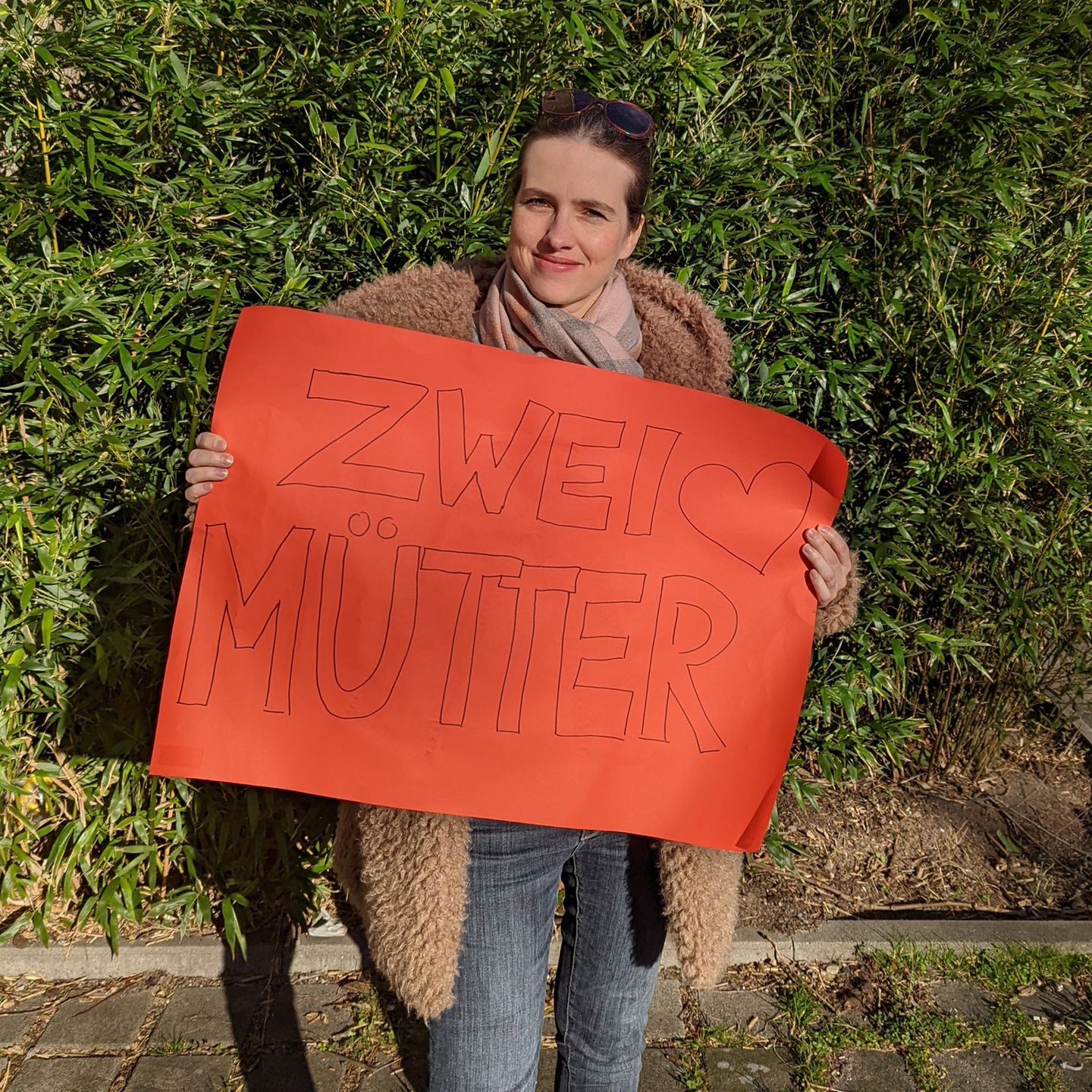 Weltfrauentag: Redakteurin Anna hält rotes Plakat mit der Aufschrift "Zwei Mütter"