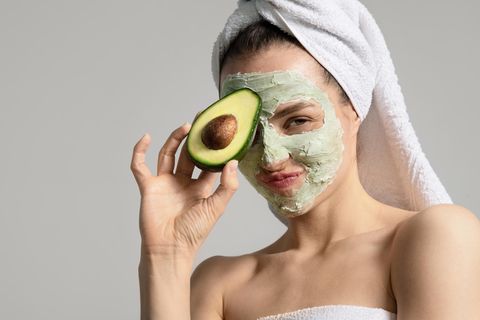 Scincare: Frau mit Gesichtsmaske aus der Haut, die eine Avocado in der Hand hält