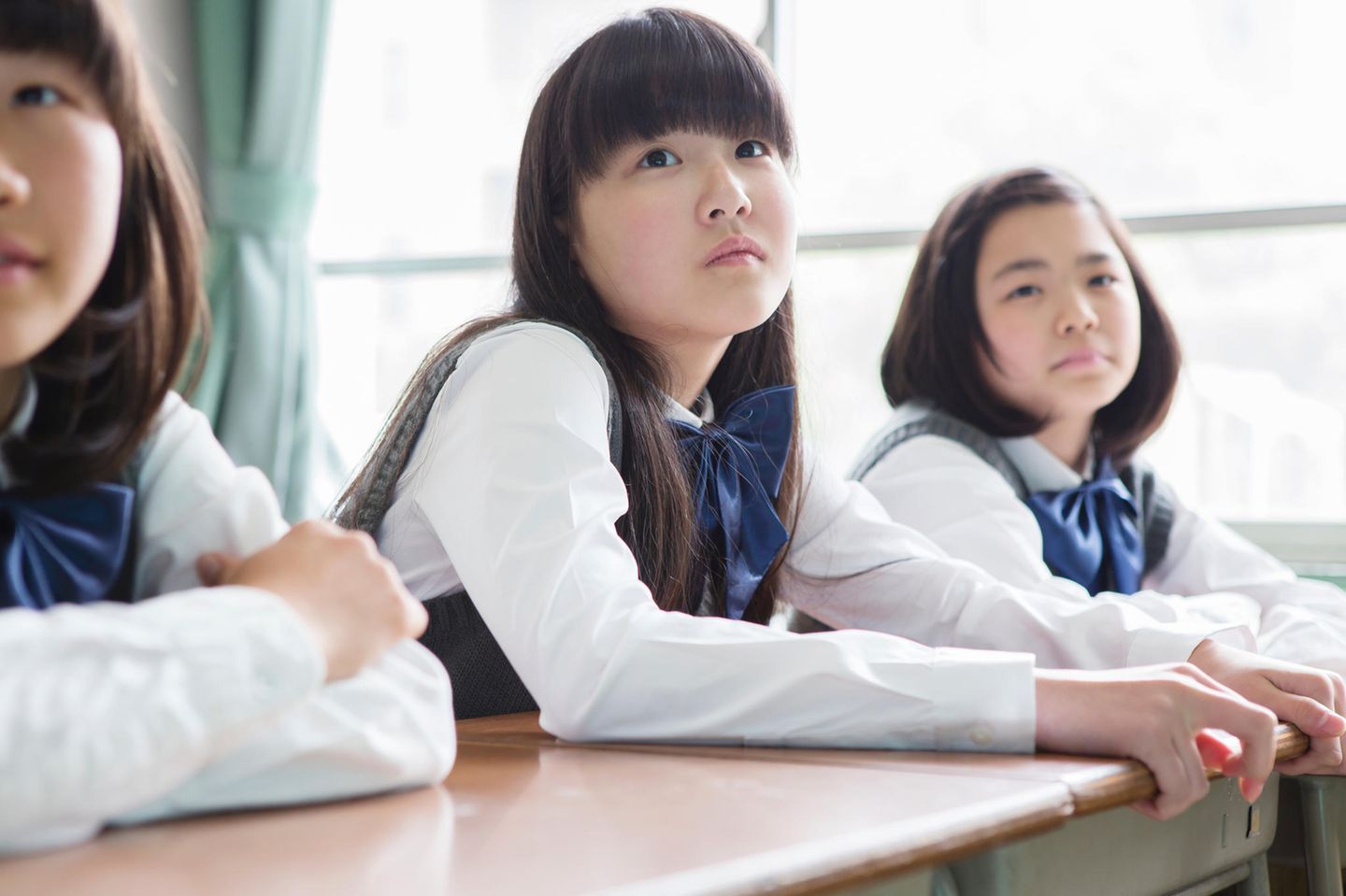 Japans Schulen und ihre strengen Regeln: 3 japanische Schülerinnen sitzen in der Klasse und schauen in die Kamera