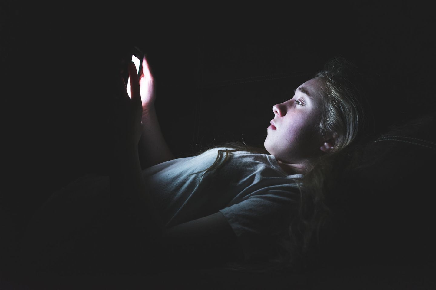 Russland: ein Mädchen liegt im dunklen Zimmer und hat ihr leuchtendes Smartphone in den Händen