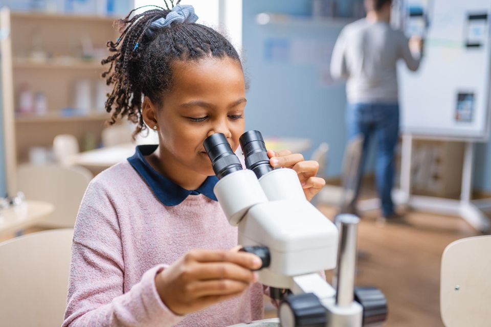 Ein Mädchen schaut im Unterricht durch ein Mikroskop