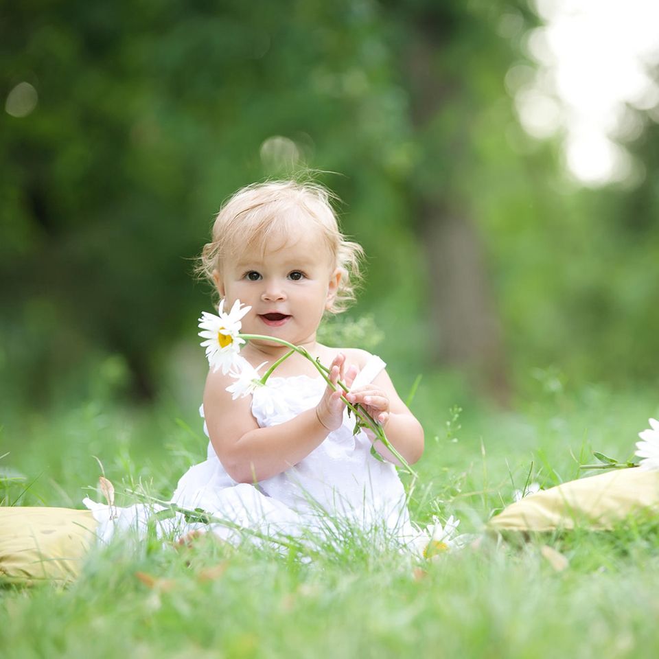 Ein Kleinkind sitzt mit einem Blumenstrauß in den Händen im Gras.