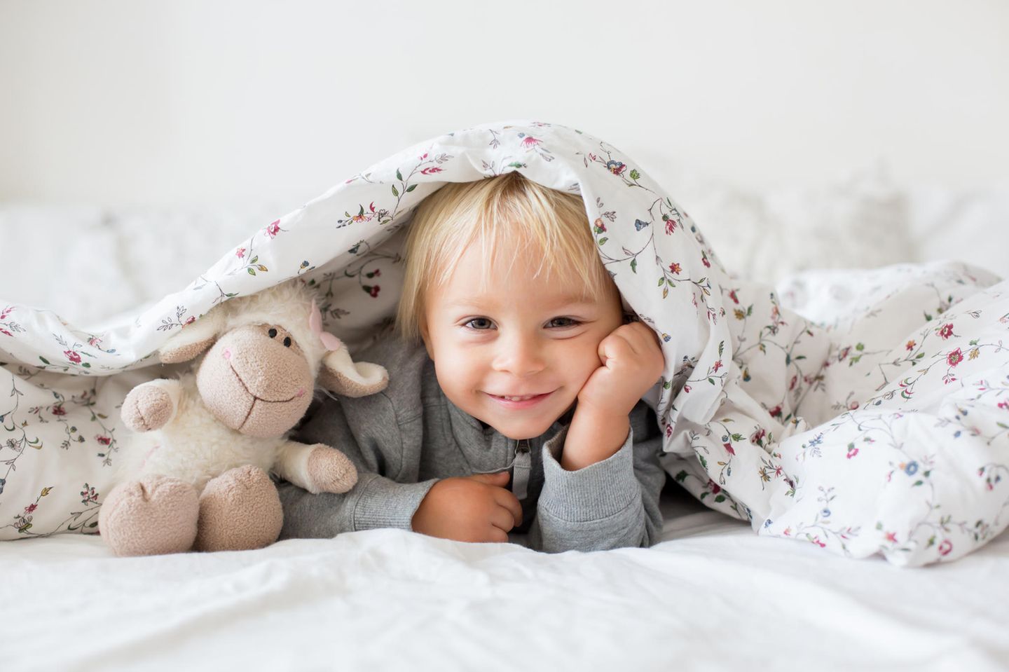 Kinder richtig aufwecken: Kind unter der Decke mit einem Kuscheltier
