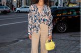 Designerin Lani Lees bringt mit ihrer gemusterten Bluse und der gelben Handtasche Spring Vibes auf die Straßen Berlins. Die beigefarbene Hose vollendet das frühlingshafte Outfit.