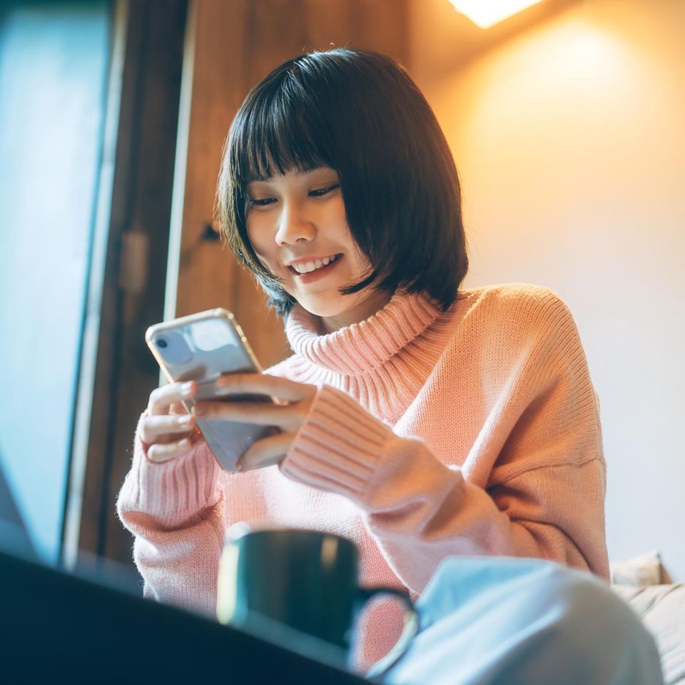 Neo-Broker: eine asiatische Frau sitzt vor ihrem Laptop mit einem Smartphone in der Hand