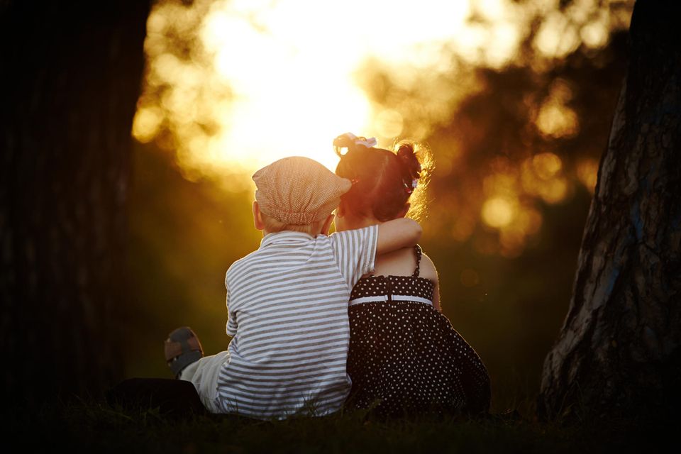 Junge und Mädchen halten sich im Arm und schauen in den Sonnenuntergang