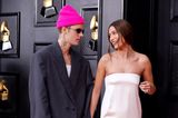 Während Justin Bieber im grauen XXL-Anzug von Balenciaga und pinkfarbener Mütze etwas zusammengeschrumpft aussieht, leuchtet seine Frau Hailey im eleganten, weißen Bustierkleid von Saint Laurent.