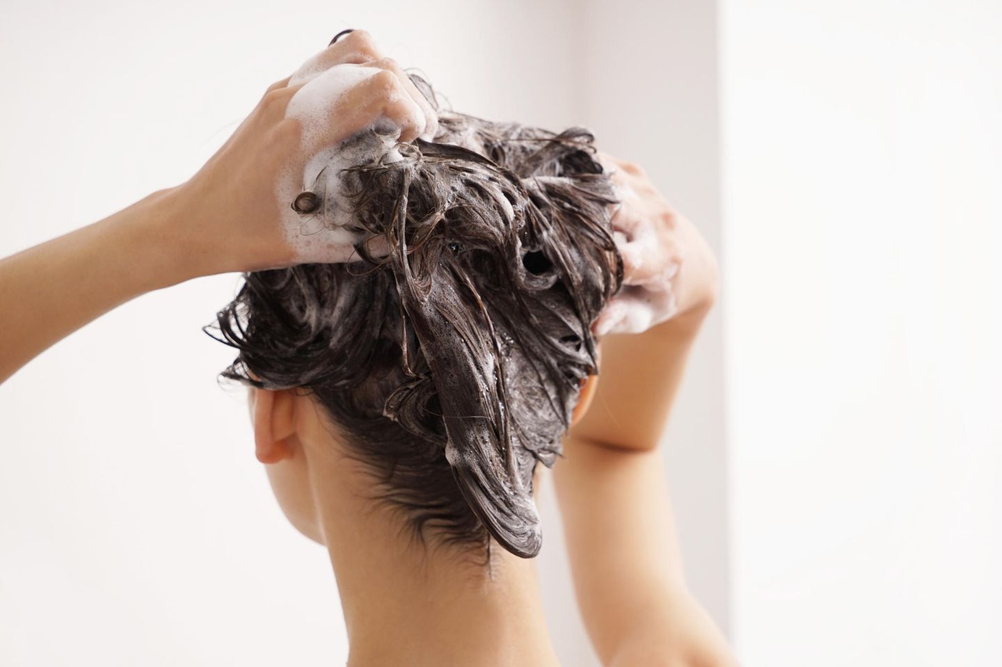 brünette-frau-wäscht-haare-mit-shampoo-gegen-fettige-haare
