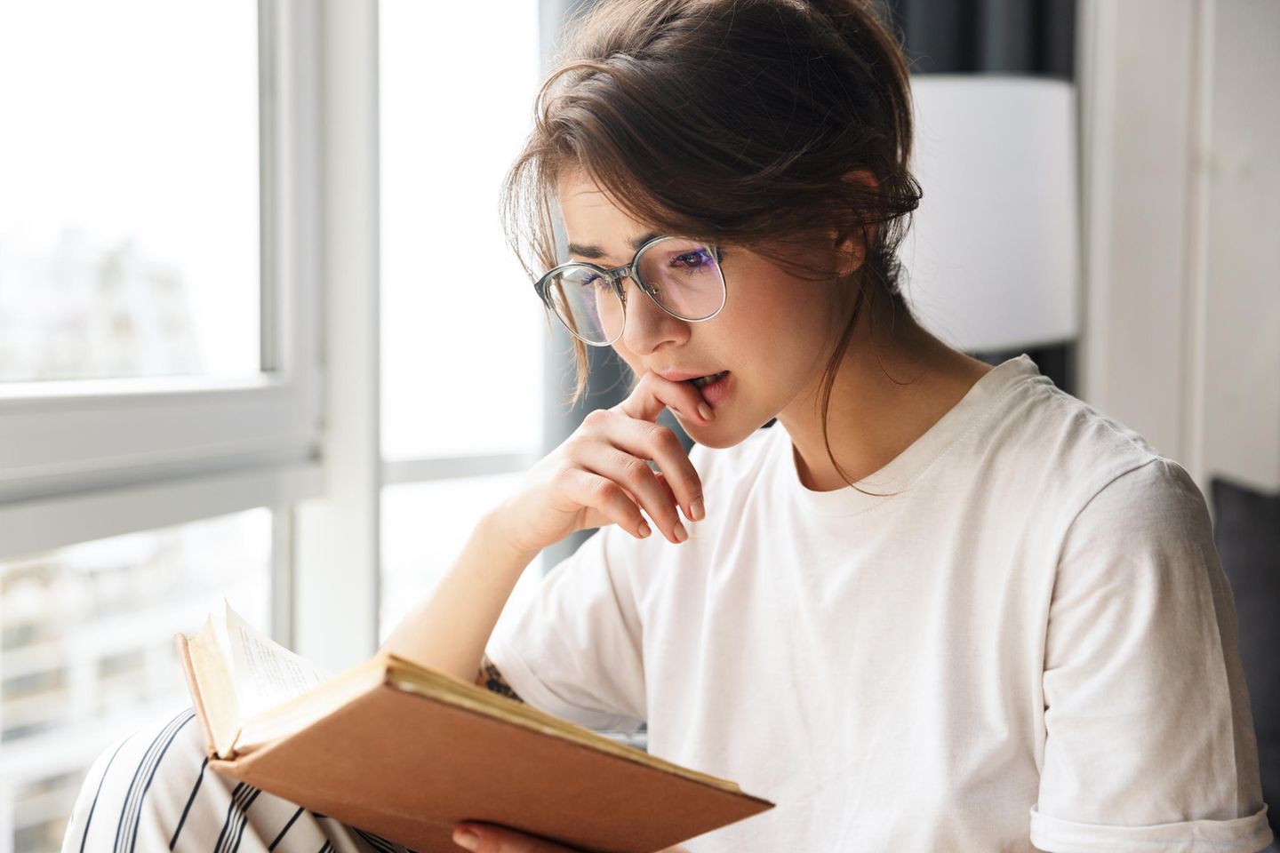 junge Frau mit Brille liest Buch gegen Liebeskummer