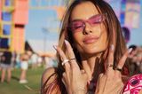 Topmodel Alessandra Ambrosio feiert mit ihrem Festival-Look die 90s und trägt unter ihrer pinken Sonnenbrille einen breiten schwarzen Lidstrich. Die Lippen sind im glossy Rosé gehalten, auf den Nägeln gibts süße Smileys. 