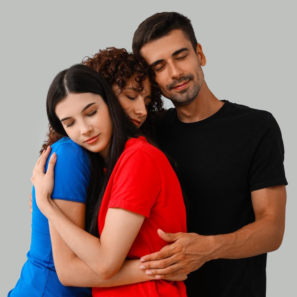 Polyamore Beziehung: Ein Mann und zwei Frauen halten sich im Arm