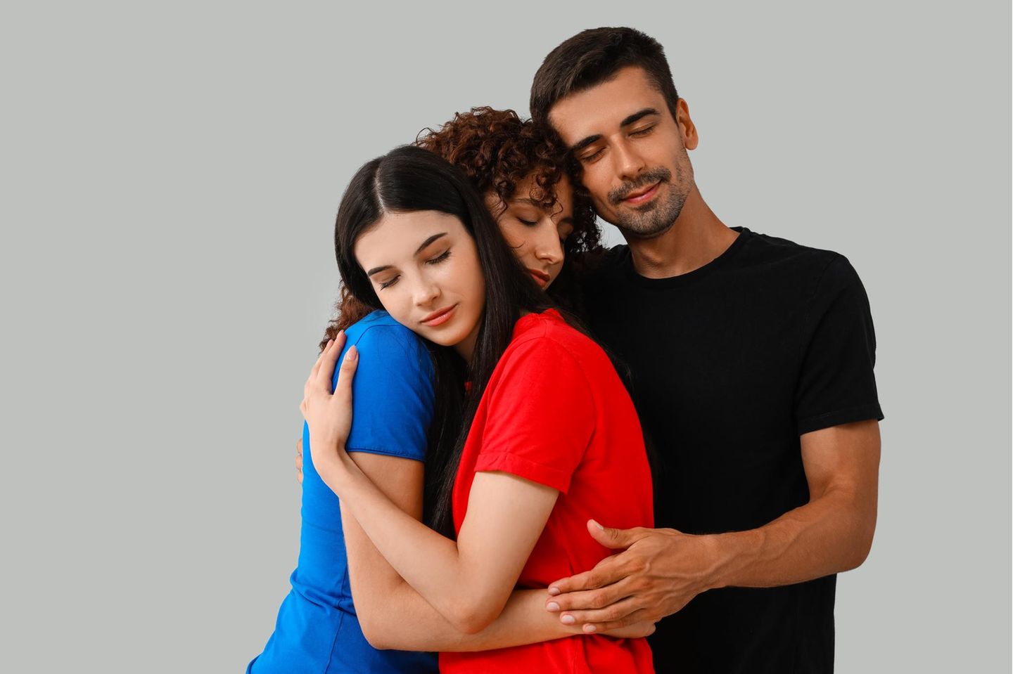 Polyamore Beziehung: Ein Mann und zwei Frauen halten sich im Arm