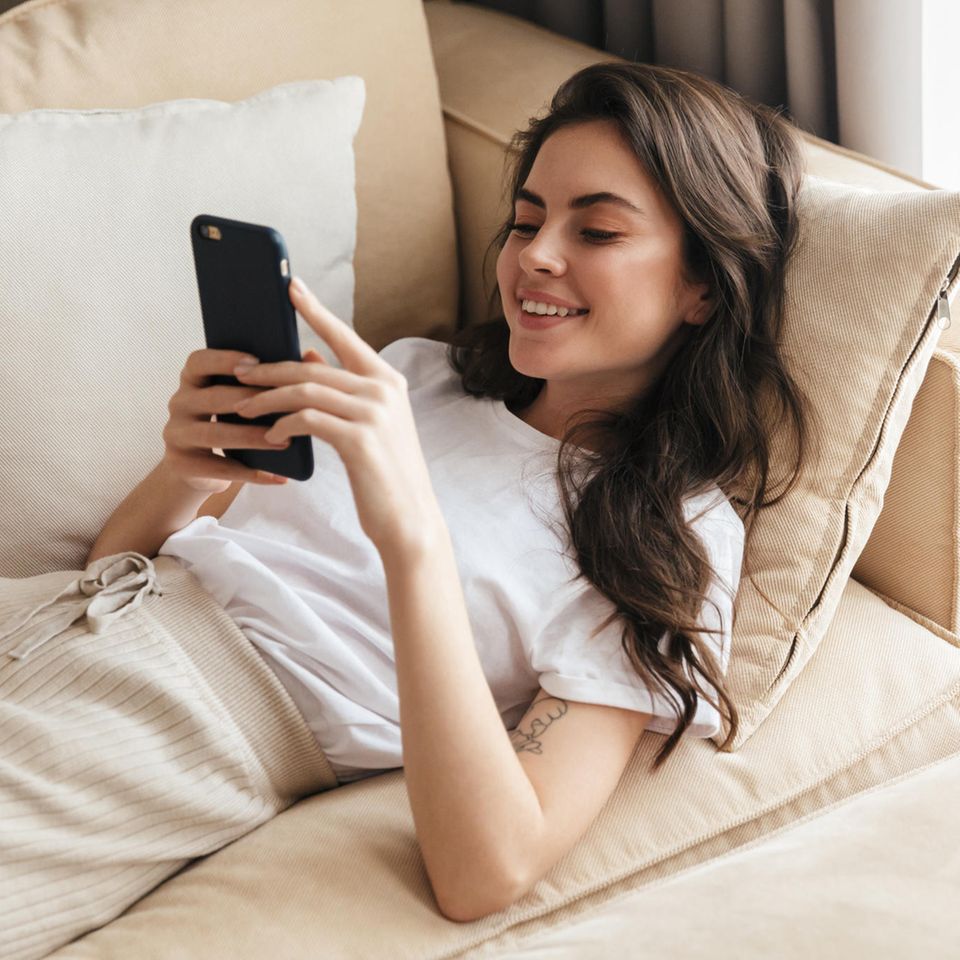 LAT-Beziehung: Frau liegt mit dem Handy auf dem Sofa
