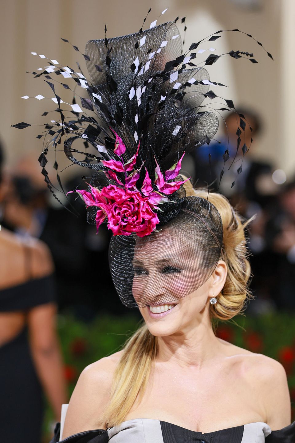 Auf dem Kopf von Schauspielerin Sarah Jessica Parker prangt eine große, pinkfarbene Blume. Doch nicht nur der Hut ist laut und bunt, der Beauty-Look mit Statement-Blush und schwarz umrandeten Augen ist ebenfalls nichts für schüchterne Menschen.