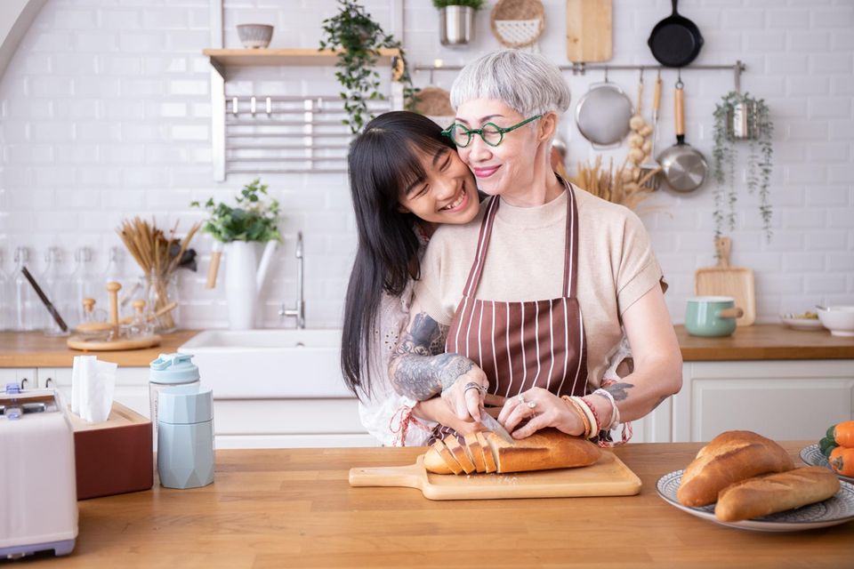 Zwei Frauen schneiden in der Küche Brot: Kohlenhydrate + Fett können dein Leben verlängern