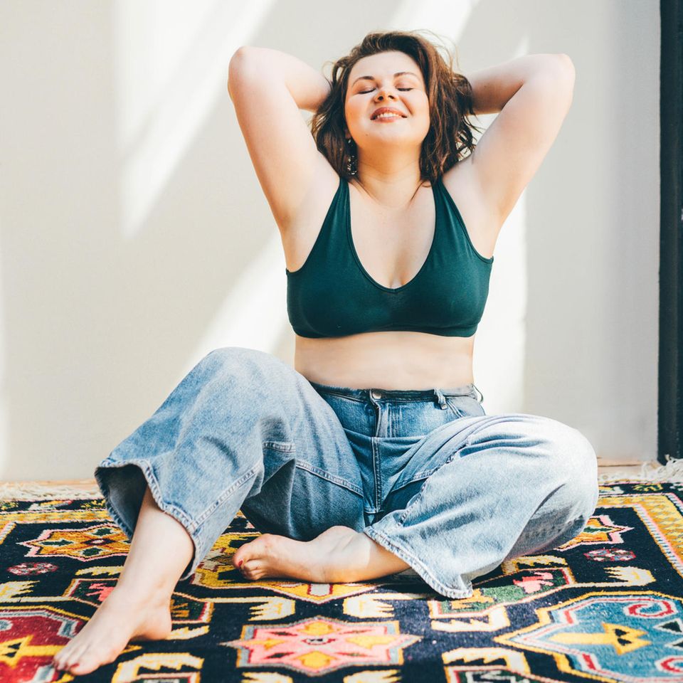 7 Pfeiler der Selfcare: Glückliche Frau sitzt auf dem Teppich