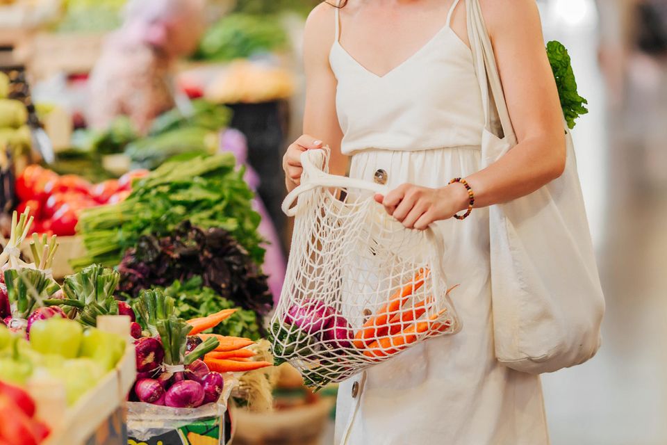 Orthorexie: eine Frau im weißen Kleid steht im Supermarkt und hält Gemüse in einem Netz
