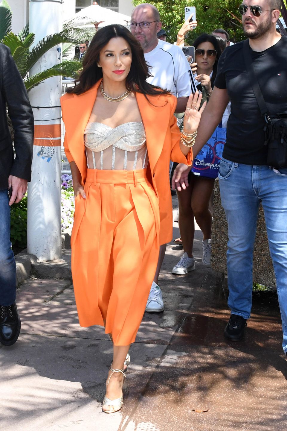 Mit großen Statementschultern und in der Trendfarbe des Sommers zeigt sich Eva Longoria auf den Straßen von Cannes. Zu einem silbernen Top kombiniert sie einen orangenen, weit geschnittenen Anzug und goldenen Schmuck.